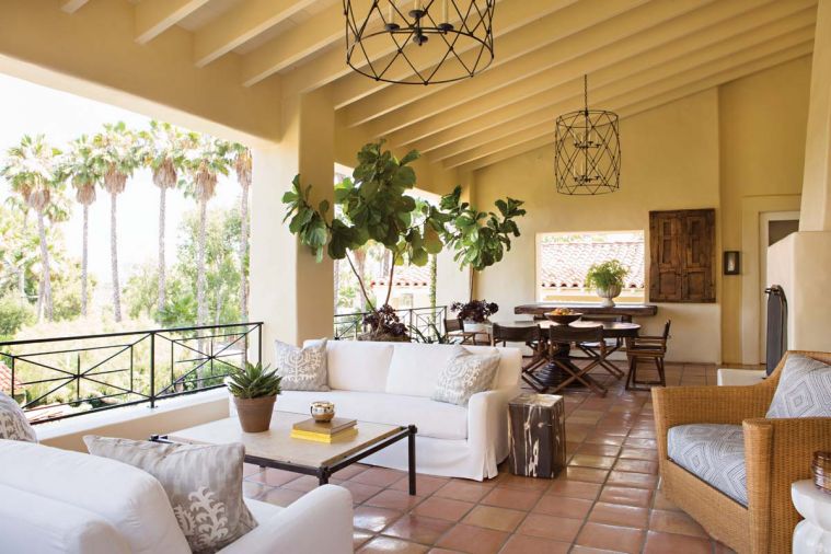 A trio of wrought iron pieces: the custom birdcage lanterns by Gearhart Ironwerks of Oregon, iron travertine coffee table and newly installed iron railing are modern touches that enhance the view when seated on the Restoration Hardware sofas. Behind the wooden salvage door lies a wine butler that delivers bottles from the cellar below. Vintage McGuire director’s chairs are refurbished with outdoor leather, while Wicker Works swivel chairs done in a Schumacher fabric plays off sofa pillows done in Travers “Tazza”.