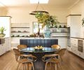 A pair of custom Gearhart Ironwerks wagon wheel bronze chandeliers crown the kitchen and adjacent sitting room to bring a touch of old Hollywood to the area. Natural Cream cabinets play off a bronze farmhouse sink, and newly painted black walnut island. The owners  Norman Cherner c. 1958 chairs and Warren Platner table imported from their former home add panache.