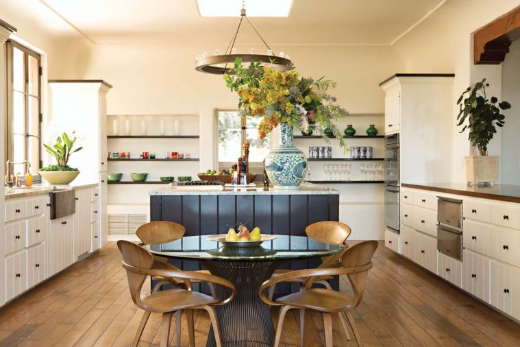 A pair of custom Gearhart Ironwerks wagon wheel bronze chandeliers crown the kitchen and adjacent sitting room to bring a touch of old Hollywood to the area. Natural Cream cabinets play off a bronze farmhouse sink, and newly painted black walnut island. The owners' Norman Cherner c. 1958 chairs and Warren Platner table imported from their former home add panache.