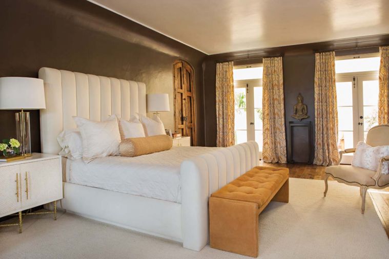 Dramatic chocolate brown walls enrobe the spacious master and sitting room. “I wanted to wrap the space in this sexy masculine color with lots of white furnishings and apricot curtains and bench,” says Joelle. The upholstered A. Rudin bed, and Michael Taylor marble side table in the seating area make lavish statement pieces. A McLean lantern “enlightens” Buddha upon a custom white oak stained ebony stand by Maison.
