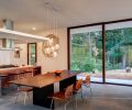 A suspended kitchen ceiling encapsulates the range exhaust hood to provide better counter task lighting, more intimacy, and a hidden place for wiring. A glass blacksplash painted red reflects the exterior surroundings, so the view is always carried outside, thus maintaining the visual flow of “interiors as part of exterior.” A Peruvian Walnut table top from Edensaw Woods in Port Townsend awaits its final legs.