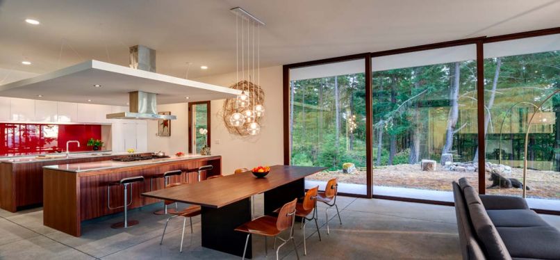 A suspended kitchen ceiling encapsulates the range exhaust hood to provide better counter task lighting, more intimacy, and a hidden place for wiring. A glass blacksplash painted red reflects the exterior surroundings, so the view is always carried outside, thus maintaining the visual flow of “interiors as part of exterior.” A Peruvian Walnut table top from Edensaw Woods in Port Townsend awaits its final legs.