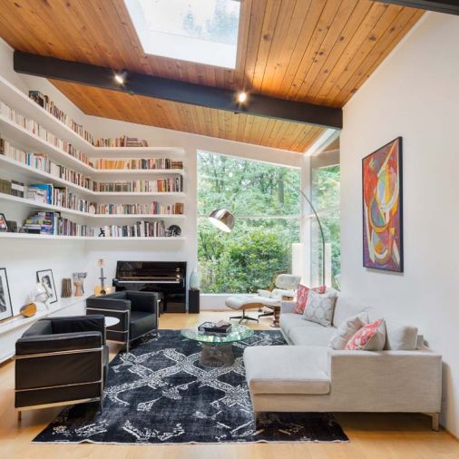 Abundant natural light floods the living room from floor-to-ceiling windows, a skylight and light from the entryway and hall. Custom shelves wrap along two sides of the living room to provide housing for the family’s large collection of books. At the bottom, a cabinet serves triple duty: its drawers hold a large collection of LP records and its top can be used for additional seating or as a display space for photographs, art and collectibles. Furnishings inspired by icons Corbusier and Eames provide comfort for the family or while entertaining.