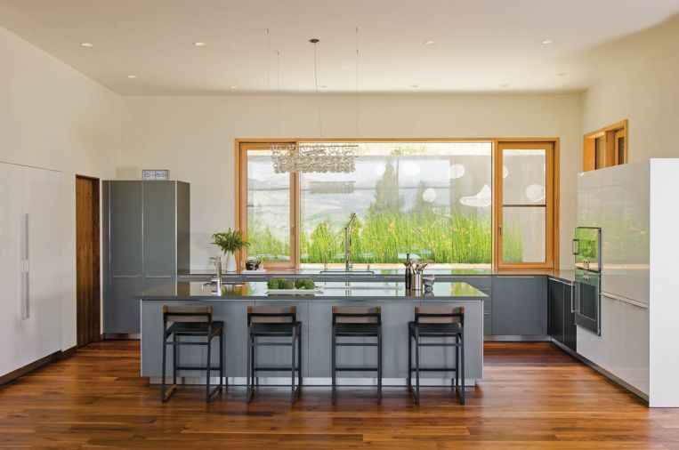 The home’s floorboards are made from walnut, a dark hardwood that looks fantastic with the spare, modern color palette chosen by the homeowners. Wood for the floors was supplied by Green Mountain Hardwoods, a local Forest Stewardship Council- certified wood flooring reseller. The home’s bulthaup kitchen features anodized aluminum cabinets and quartz countertops. Diego barstools are by Token NYC and a Giogali chandelier by Vistosi hangs above the island.