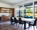 The dining area is found in the open communal area, with views out to the spacious backyard, which includes a large patio. Walnut bar cabinetry ties to the adjacent kitchen and includes a moon shadow (gray back painted) backsplash relating to the custom table with concrete skim coat, beverage cooler, wine rack and open glass shelving. Glass pendant chandelier features LED glass bulbs that do not block the view.