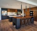 To keep the design contiguous with good visual flow, the use of dark walnut cabinetry along the storage wall was trimmed with a band of stainless steel that reiterates the horizontal stainless steel straps seen on the 10’ barn door with Krownlab hardware leading into the study at left. A breakfast area with appliances to make everything from smoothies to toasted bagels disappears behind receding doors for the rest of the day.