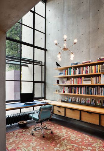 The dove gray concrete wall on the north side of the house does an amazing job as a reflector, bringing bright but diffuse natural light throughout the home. The shelving in this work room was custom-designed by RHO Architects, and a blue desk chair from Knoll provides contrast against a warm, salmon-colored area rug from the homeowners’ collection.