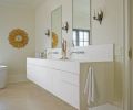 The bathroom lavatory was also custom-designed by Janice Viekman, using solid surface construction that mimics Corian cabinetry. Vola plumbing fixtures were sourced from Best Plumbing, and the wall sconces came from Century Lighting. The overall effect in the bathroom is simultaneously soothing yet visually engaging thanks to the custom-cut shutter and its reflection in the mirrored antique wardrobe.