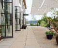 Canvas awnings can be unrolled to dapple the entry garden and patio with shade on hot days. Inside, full-length curtains provide visual and material repetition, creating a strong link between the interior and the garden to create a room-like effect. The garden echoes the symmetrical lines of the home by using a formal style. The exterior of the building is hand-troweled stucco with integral color.