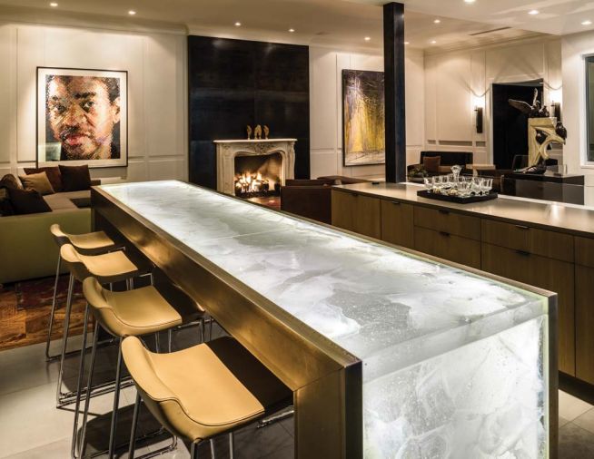 A blackened steel panel sets off a traditional fireplace surround on the penthouse floor. A cast glass bar top fabricated by Mike Danielson Studio is paired with Claudio Bellini bar stools. At right, doves perch on an architectural fragment.