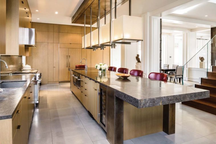 The new open plan is visible from this angle of the kitchen. Beautiful Italian marble was used for kitchen countertops and powder rooms. Stuart Silk and his team created the 18’ long island design of polished and glazed Italian marble and burnished nickel legs and ends. The powder room door is concealed within the wall of oak cabinetry.