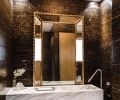 Custom carrara marble vanity and natural stone walls, gilded mirror and chandelier by GCW distinguish the first of two powder rooms