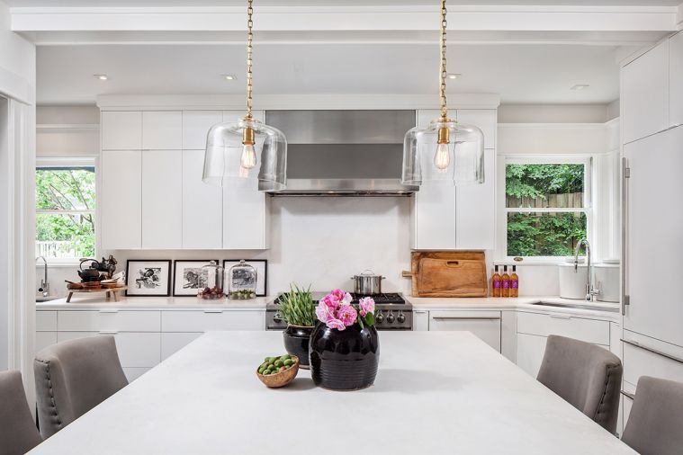 Hester fully remodeled the kitchen, which is located towards the back of the home. “In the old
days, the kitchen was not important,” she explains.
“Because that was where the maid was cooking.” Now, the kitchen features a clean, modern aesthetic. Natural Pental marble gives the all-white kitchen a soft, natural feel. The grey upholstered barstools were sourced from Hickory Chair, while clear glass pendant lights are from Visual Comfort. A Sub-Zero refrigerator and Wolf range and hood give even the appliances a streamlined look.