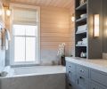 Cool marble finishes in the
master bathroom contrast with the warm tones of the spruce paneling. Hardware, including drawer pulls, faucets, and wall mount lamps, is all bronze to continue the beach-inspired look.