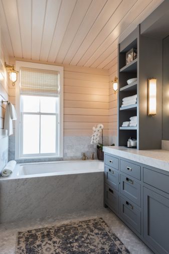 Cool marble finishes in the
master bathroom contrast with the warm tones of the spruce paneling. Hardware, including drawer pulls, faucets, and wall mount lamps, is all bronze to continue the beach-inspired look.